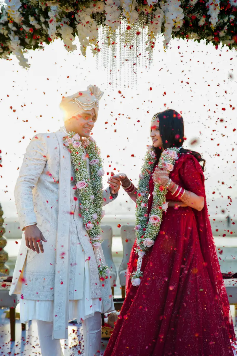 A bride and groom smiling at each other beneath flowers as rose petals fall around them